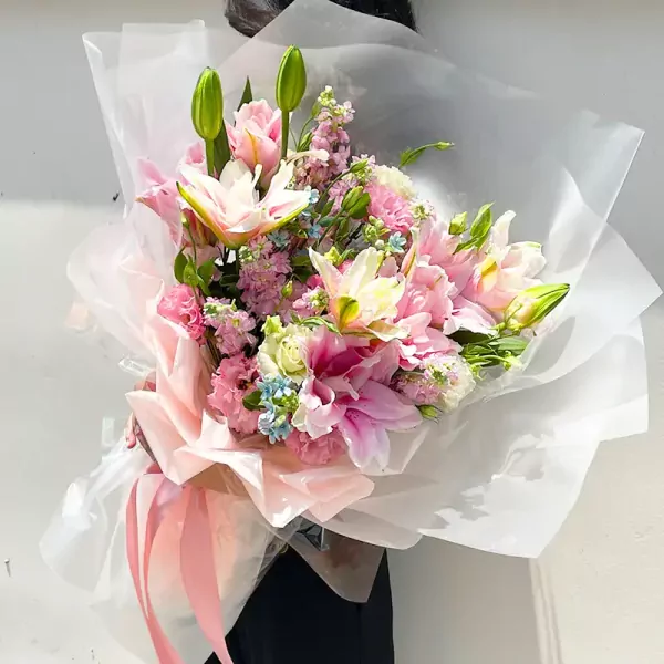 Pink lily bouquet with delphinium and star flowers, wrapped in sheer paper and tied with ribbon.