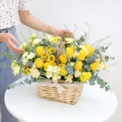 Basket of yellow roses, sunflowers, and carnations with eucalyptus leaves.