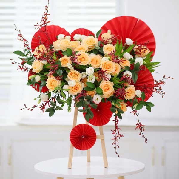 Floral arrangement of peach roses, white lisianthus, and red accents on a wooden stand.