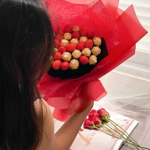 Choco Berry bouquet with strawberries and Ferrero Rocher chocolates, wrapped in red paper, with red roses nearby.