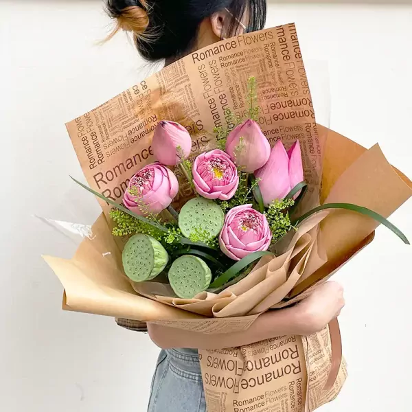 Pink lotus bouquet with lotus seed pods and decorative greenery, wrapped in brown paper.