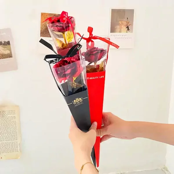 Two gold-dipped roses in red and black wrappers held by hands.