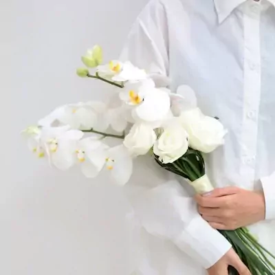 White orchid and rose bridal bouquet held by a person in a white shirt.