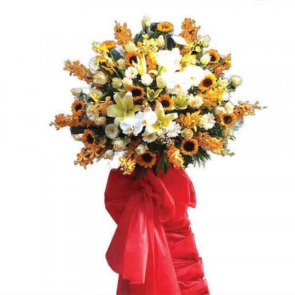 A large, grand floral arrangement of sunflowers, lilies, and orchids with a red ribbon.