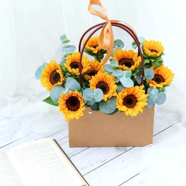 A brown paper gift bag filled with sunflowers and eucalyptus.