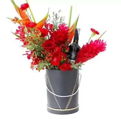 A round box arrangement of red flowers with a bottle of red wine.