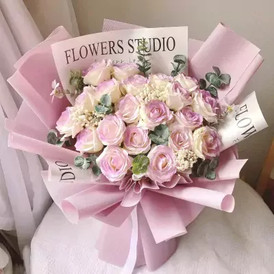 Pink and white roses in a bouquet wrapped in pink paper with text that says "FLOWERS STUDIO".