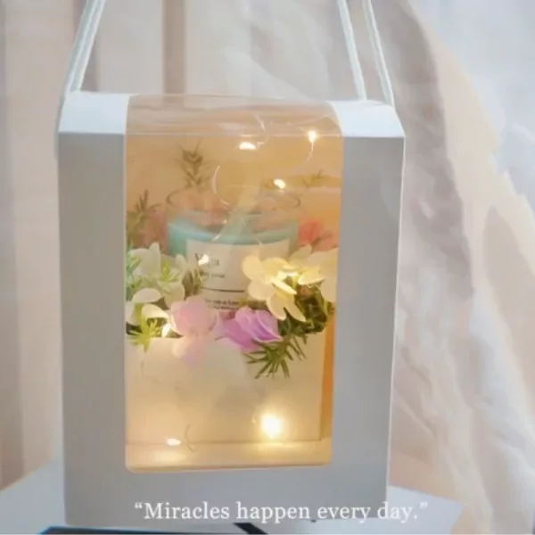 A gift box with a scented candle and flowers, decorated with fairy lights.