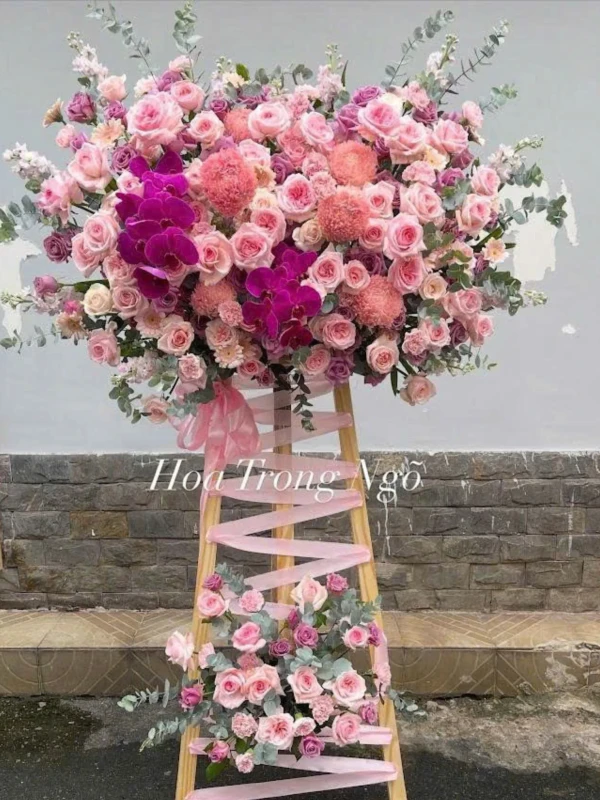 Pink and purple floral arrangement on a wooden easel, featuring roses, orchids, and other blooms.