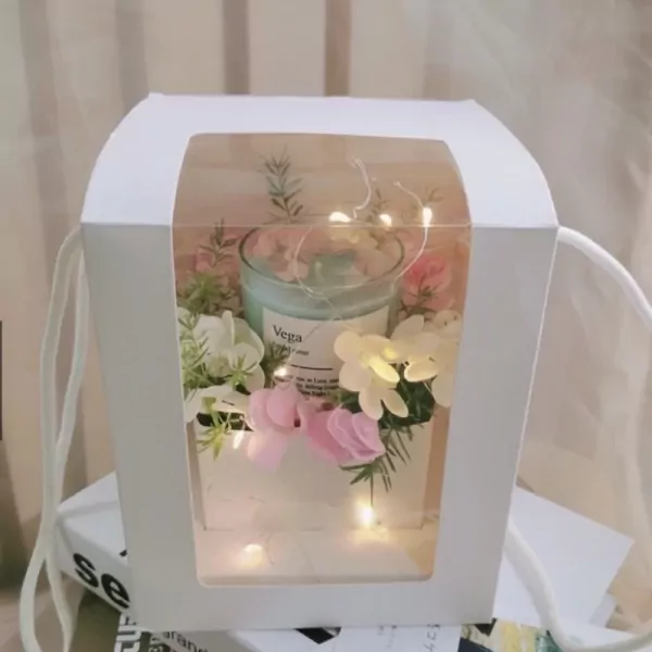 White gift box with a candle and flowers, illuminated by fairy lights.