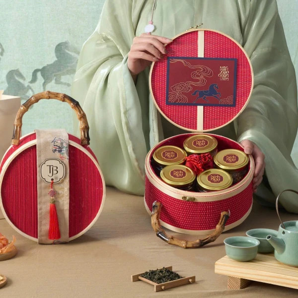 Red woven gift basket with bamboo handle, holding jars of treats and tea, featuring a horse design lid.