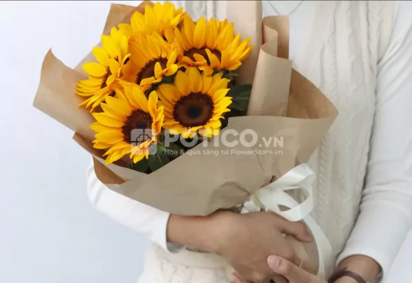 A bouquet of sunflowers wrapped in brown paper, tied with a white ribbon.