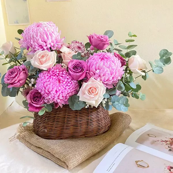 Basket of pink and purple chrysanthemums and roses with eucalyptus leaves.