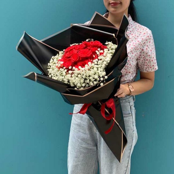 Woman holding a bouquet of red roses and baby's breath, wrapped in black paper.