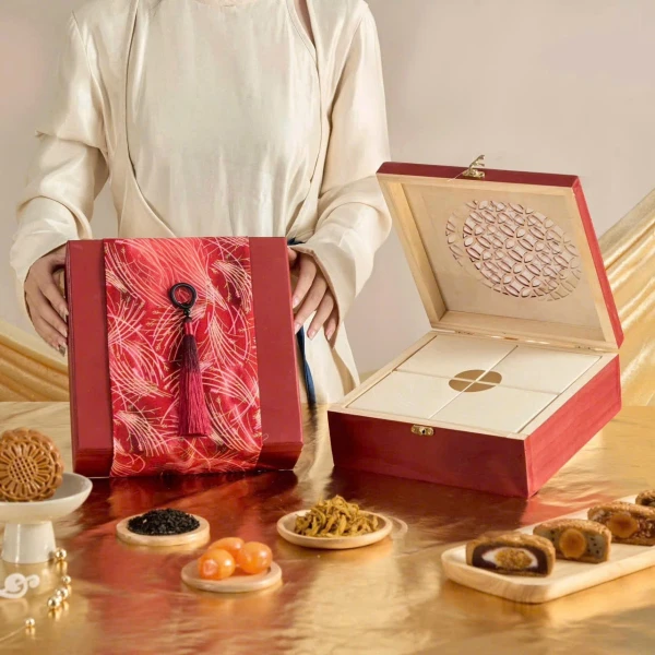 Red gift box with mooncakes, a wooden box, and ingredients on a gold surface.