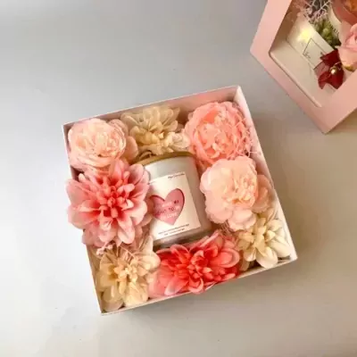 Gift box with a scented candle and pink and peach artificial flowers.