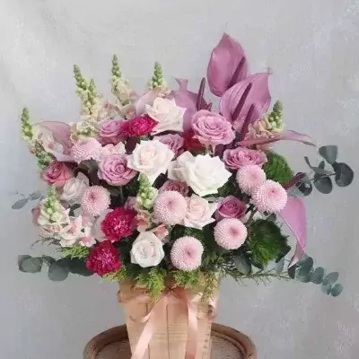 A wooden box of pink and white roses, chrysanthemums, carnations, and foliage.