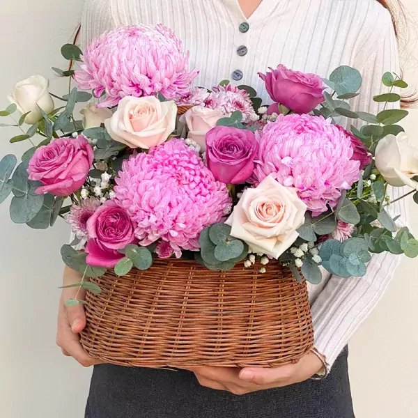 Pink and purple flowers in a woven basket, held by a person.