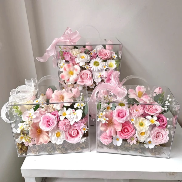 Clear boxes filled with pink and white artificial flowers, decorated with pink bows.