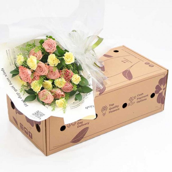 Bouquet of pink and yellow roses with green foliage in a gift box.