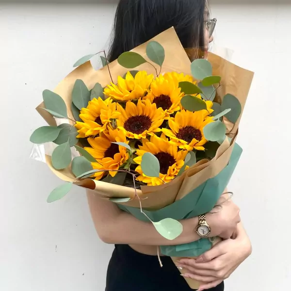 Bouquet of sunflowers and eucalyptus leaves, wrapped in brown and green paper.