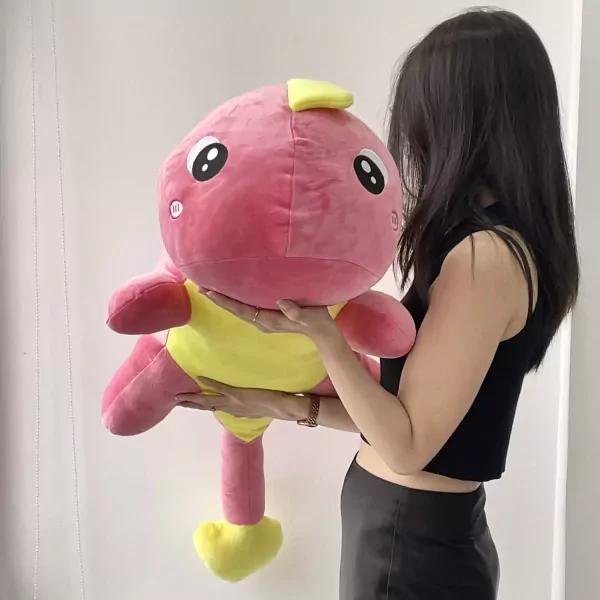 A person holds a large, plush pink dinosaur with a yellow belly and feet.