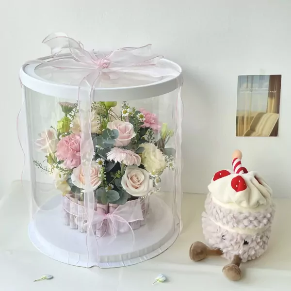 Round clear box with pink flowers and money stacked around the base, next to a plush cupcake toy.
