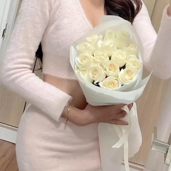 Woman in a pink fluffy outfit holding a bouquet of white roses.