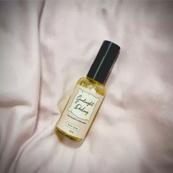 A room spray bottle labeled "Goodnight Darling" rests on a soft pink fabric.