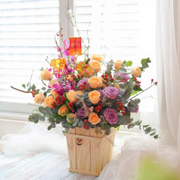 Wooden box of peach and purple roses, purple orchids, and mini lanterns.