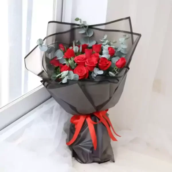 A bouquet of red roses wrapped in black paper with a red ribbon.