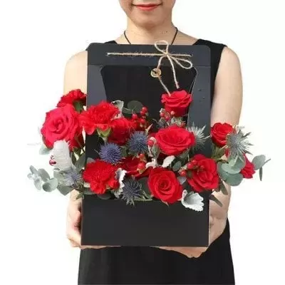 Woman holding a black box with red roses, carnations, and thistles.