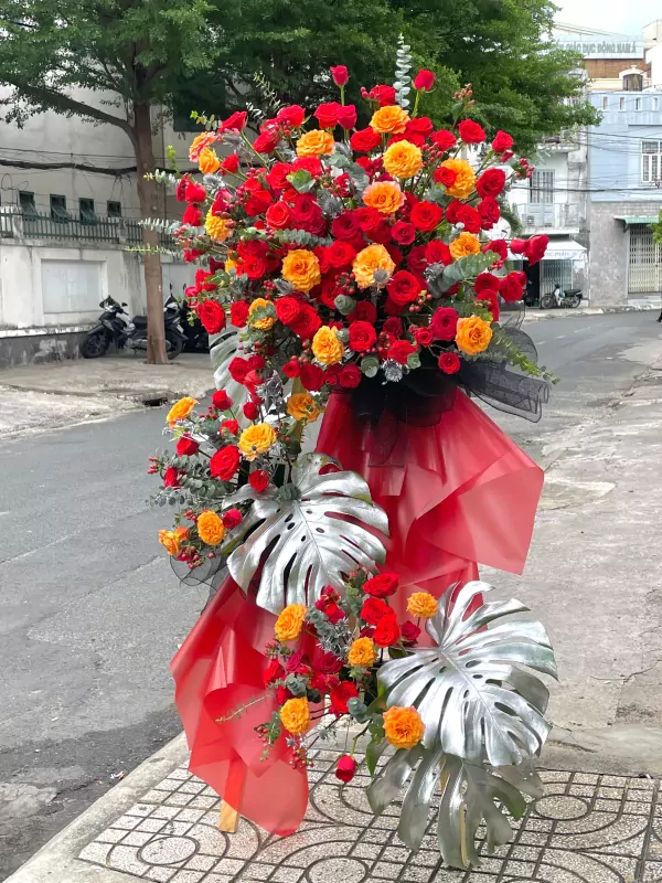 A large flower stand with red and orange roses, silver monstera leaves, and red fabric.
