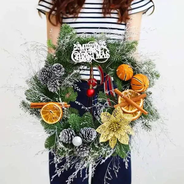 Christmas wreath with pine cones, dried oranges, cinnamon sticks, and "Merry Christmas" sign.