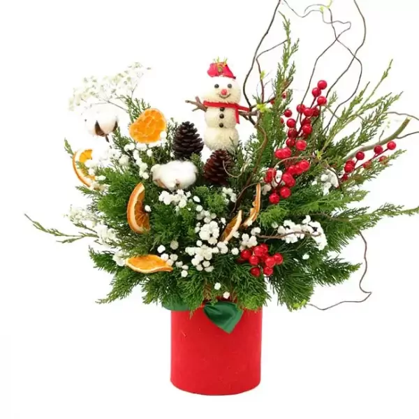 Christmas arrangement in a red vase with a snowman, pinecones, berries, and dried oranges.