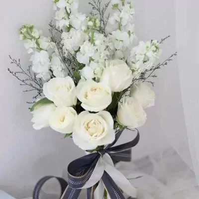 White roses and stock flowers in a bridal bouquet with a dark blue and white ribbon.