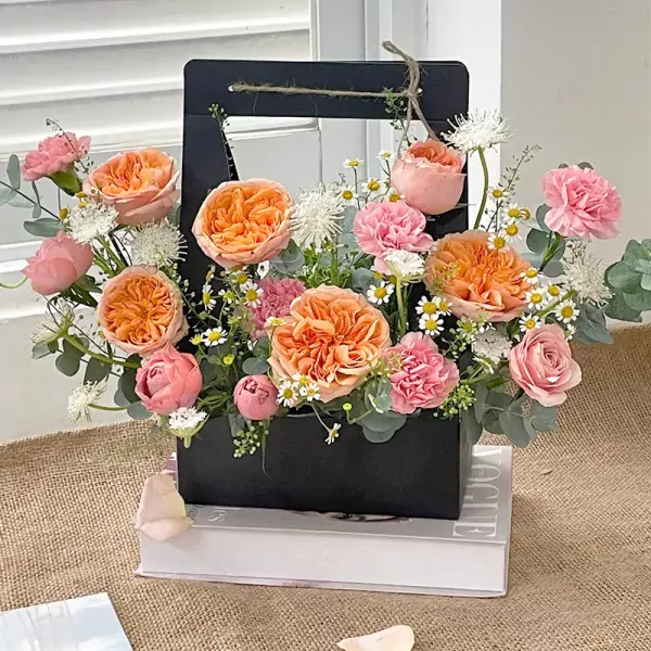Orange and pink roses, carnations, and daisies in a black floral box.