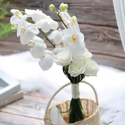 White orchids and roses in a bridal bouquet arrangement with a wicker basket.