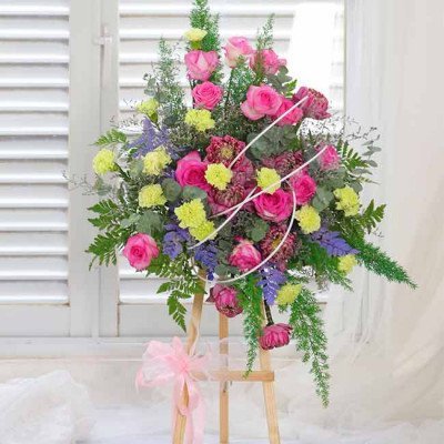 Pink roses, lotus, and green carnations on a wooden stand with a pink bow.