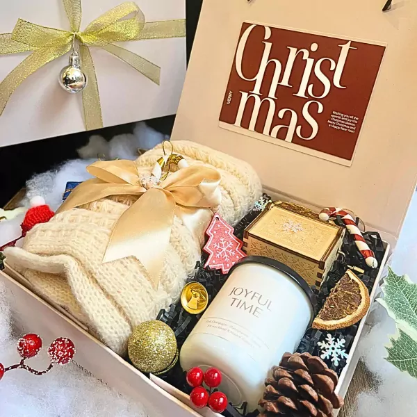 Christmas gift box with knitted scarf, candle, candy cane, and decorative ornaments.