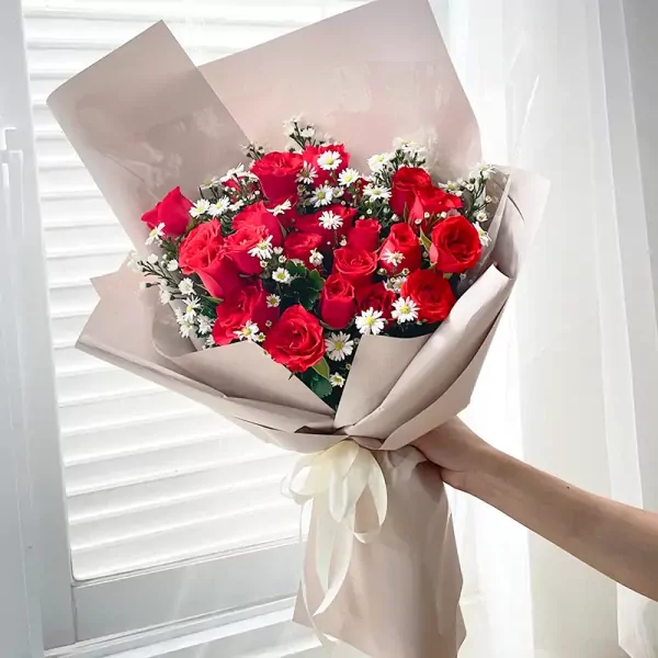Bouquet of red roses with white filler flowers, wrapped in beige paper and tied with a cream ribbon.