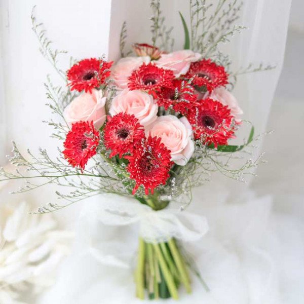 Wedding bouquet with red gerberas and light pink roses, tied with a white ribbon.