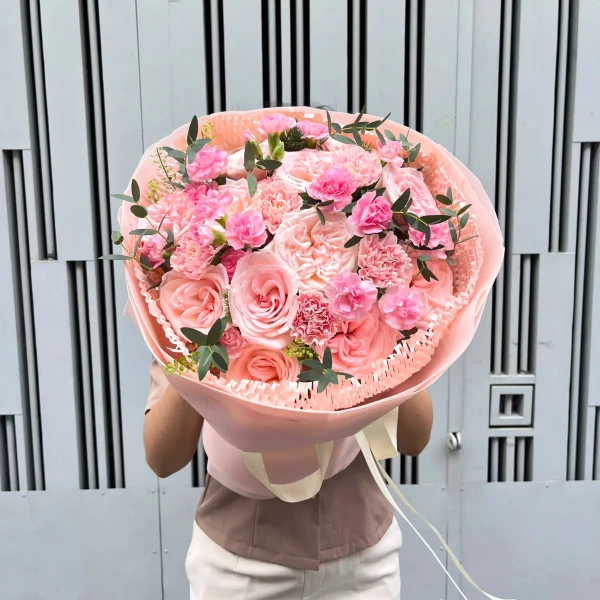 Pink roses and carnations in a soft pink bouquet with ribbon accents.