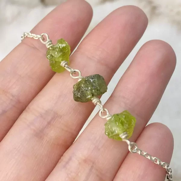 A silver bracelet with raw, green stones on a hand.