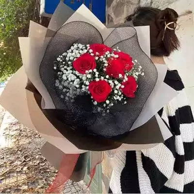 Bouquet of red roses with baby's breath, wrapped in black mesh and light-colored paper.