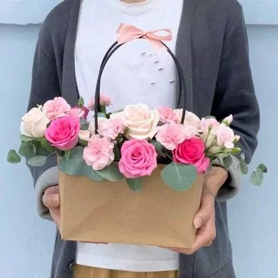 Floral arrangement in a brown paper basket with pink and cream roses, carnations, and greenery.