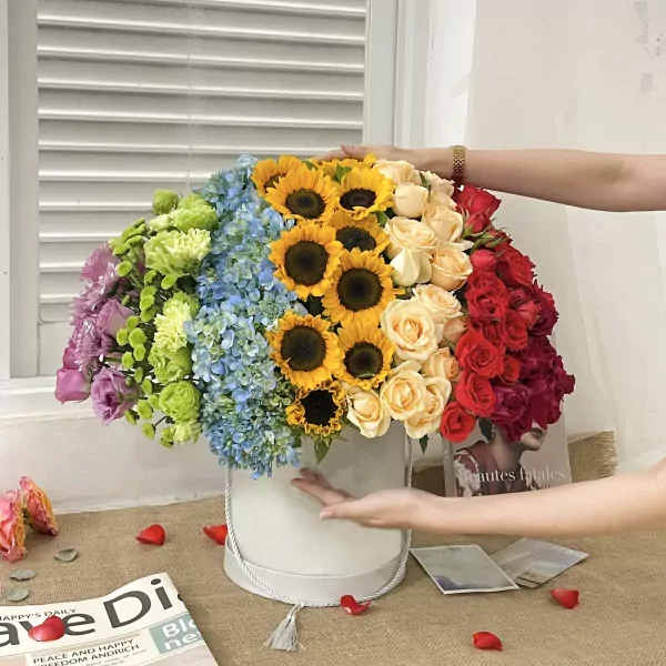 Vibrant rainbow flower box with roses, sunflowers, hydrangeas, and greenery.
