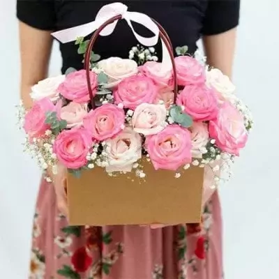 Basket of pink and cream roses with baby's breath, tied with a white ribbon.