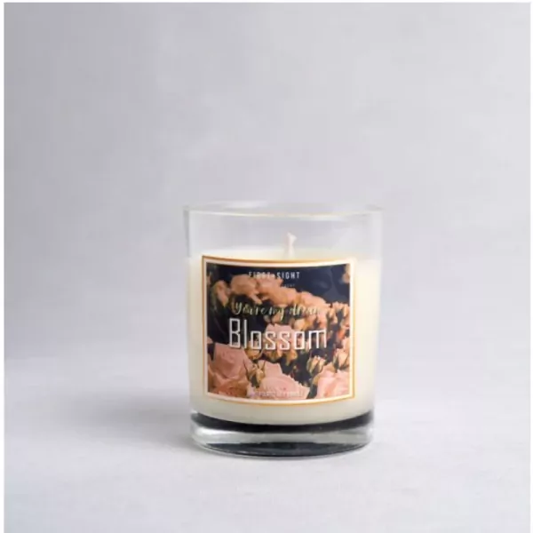A white candle with a "Blossom" label featuring pink flowers in a glass jar.