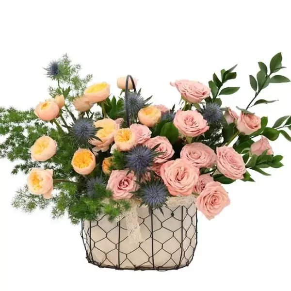 A floral arrangement in a wire basket with pink roses, yellow roses, and blue thistle.